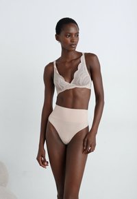 Bralette de renda bege com um design de decote em V e padrão floral, combinado com cuecas de cintura alta, lisas e de cor nude.