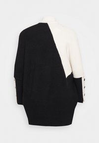 Cardigan a maglia con design asimmetrico bianco e nero, texture a coste, collo alto e bottoni decorativi sulle maniche.