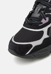 Černá sportovní bota ze síťoviny a semiše, se stříbrnými detaily a strukturovanou podrážkou. Tkaničky jsou tmavě šedé.