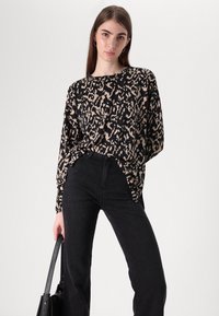 Black and beige flowing top with a bold animal print, long sleeves, and a relaxed fit, paired with high-waisted dark jeans and a black bag.