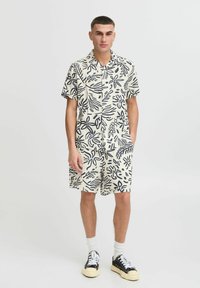 Camisa de manga corta con cuello y pantalones cortos a juego en crema con patrones de hojas en azul marino, fabricada en tejido ligero, con cierre de botón y bolsillos laterales.