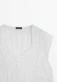 Blouse blanche à manches courtes avec un décolleté en V, des détails froncés, et un tissu léger texturé. Présente une étiquette noire au niveau du col.