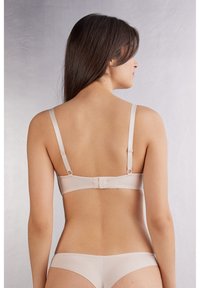 Naadloze nude bh met verstelbare bandjes, brede rugband, haaksluiting en een gladde textuur. Minimalistisch ontwerp zonder versieringen.