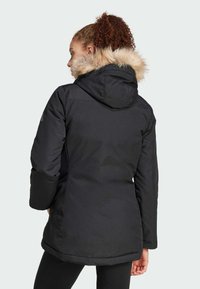 Black parka jacket with a fur-lined hood, featuring a sleek design, long sleeves, and a curved hem. Smooth texture with durable material.
