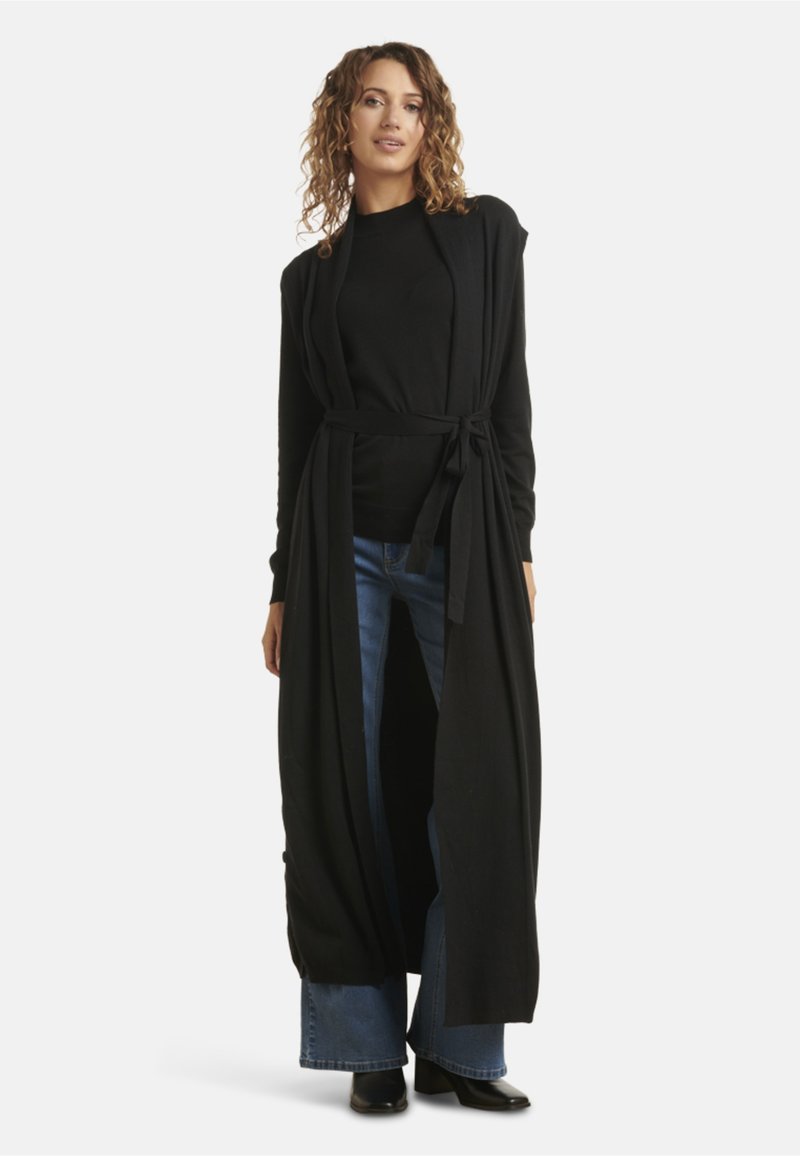 Black long cardigan made of soft fabric, featuring an open front, tie belt, and long sleeves, paired with a black top and wide-leg jeans.