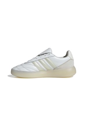 Witte Adidas sneaker met drie lichtbeige strepen, veters aan de voorkant, gestikte details en een doorschijnende beige zool, zijaanzicht.