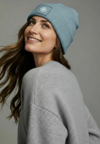 Blue ribbed beanie made of knit material with a textured finish, featuring a square patch with a compass design on the front.