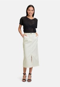 Haut noir à manches courtes perforé associé à une jupe midi crème avec une fente avant et des poches latérales, complété par des sandales noires à lanières.