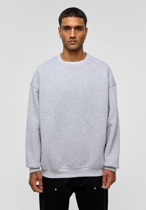 Grijze oversized sweatshirt van zacht materiaal, met een ronde halslijn en verlaagde schouders. Gecombineerd met zwarte broek.