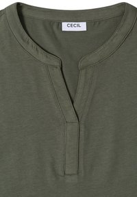 T-shirt vert olive avec un col rond, une fente courte sur le devant et des coutures visibles, avec une étiquette blanche portant le texte « CECIL » à l'intérieur du col.