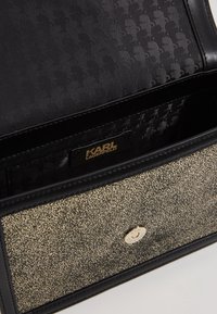 Otwarta teksturowana czarno-złota torebka Karl Lagerfeld ukazująca markowe wnętrze i zapięcie na magnes.