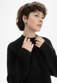 Schwarzer, gerippter Pullover mit höherem Ausschnitt und langen Ärmeln. Der Stoff hat ein strukturiertes Muster und erscheint weich und elastisch.