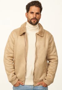 Zipperjacke aus tanfarbenem Wildleder mit weichem, braunem Kunstfellkragen, gerippten Bündchen und Seitentaschen, kombiniert mit einem cremefarbenen Rollkragenpullover.