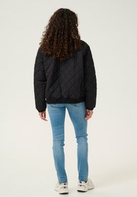 Veste matelassée noire avec une taille ajustée, des poignets côtelés et un col haut, associée à un jean fitted bleu clair et des chaussures de sport.