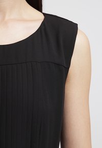Top nero senza maniche con scollo rotondo, texture plissettata e finitura liscia. Il tessuto sembra leggero e morbido.