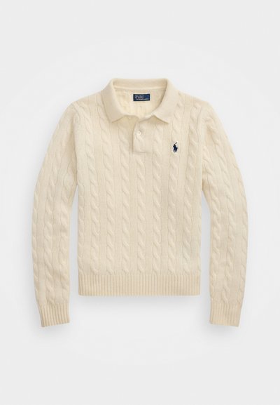 Kremkrāsas adīts polo krekls ar virvju rakstu, ribotām piedurknēm un apakšmalu, pie kura ir maza tumši zila emblēma kreisajā krūtī.