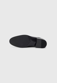 Mustad mustre saapad, millel on sile nahast pealis ja kummist tald. Omab ümmargust varvast ja minimalistlikku disaini, ilma nähtava brändita.