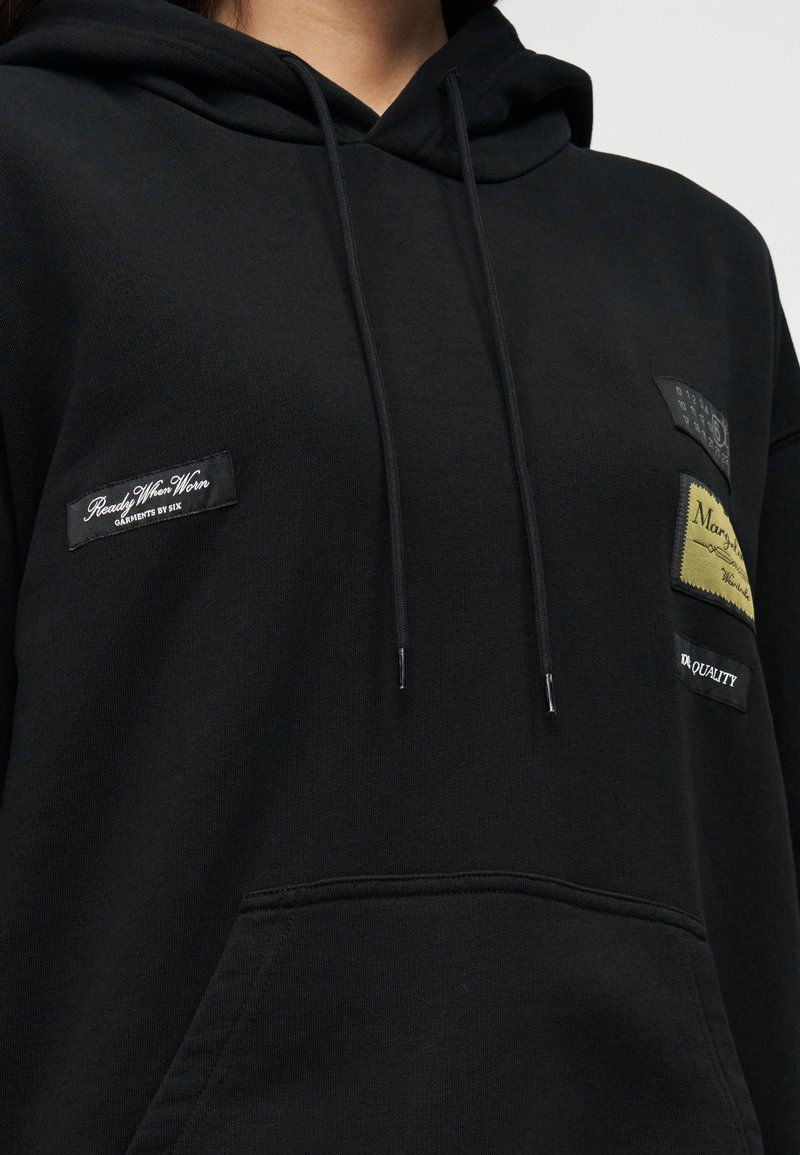 Black hoodie made of cotton blend fabric with a front pocket, featuring various colored patches and drawstrings at the hood.