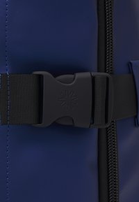Mørkeblå vanntett bag med svart plastspenne og glidelås, med svart søm og en teksturert overflate for økt holdbarhet.
