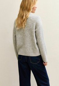 Maglione grigio con finitura testurizzata, orlo a coste e spalle rilassate, abbinato a pantaloni in denim scuro, visto da dietro.