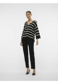 Gestreifte schwarz-weiße V-Ausschnitt-Bluse mit weiten Ärmeln kombiniert mit schwarzen Slim-Fit-Hosen und spitzen schwarzen Absätzen. Sanfte Stofftextur.
