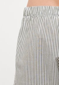 Shorts rayés avec une taille élastique, présentant des rayures verticales alternant entre le blanc et le vert olive. Fabriqués en tissu léger.