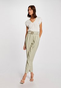 Witte V-hals top met korte mouwen, gecombineerd met lichtgroene high-waisted broek met een geraffineerde tailleband en een gouden gespriem.