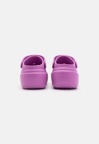 Zoccoli viola con un esterno strutturato, cinghie posteriori e un design perforato. Presentano un logo impresso e una forma ergonomica liscia.