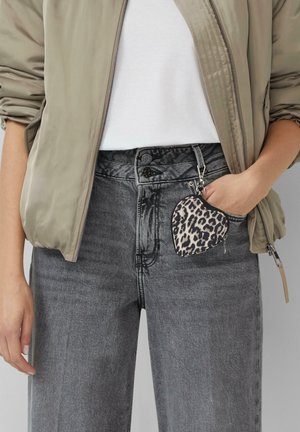 Lichtgrijze bomberjack over een wit t-shirt, gecombineerd met hoog-getailleerde grijze jeans. Een hartvormige luipaardprint pouch hangt aan de tailleband.
