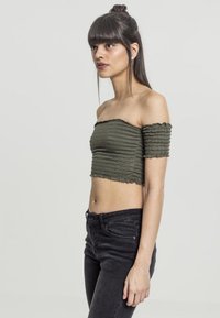 Oliven grønn av skulderen crop topp med rynket tekstur; korte, flate ermer. Brukt sammen med svarte tettsittende jeans.