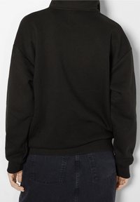 Svart sweatshirt med hög krage, lös passform och ribbade muddar. Tyget ser mjukt ut utan synliga mönster eller detaljer.