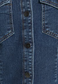 Jeansjacka med blått tyg, knapprättningar och dubbla bröstfickor med kontrasterande sömmar.