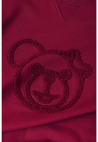 La tela de sudadera roja presenta un diseño de cara de oso texturizada y suave bordada en el centro, destacando los detalles sin ningún adorno.