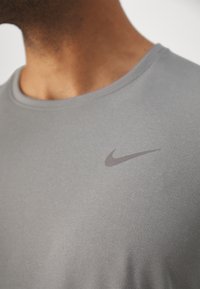 Camiseta deportiva gris hecha de tela lisa y ligera. Presenta un sutil logo de Nike en gris oscuro en el pecho. Cuello redondo.