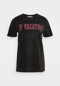 Czarny, krótki rękaw, bawełniany T-shirt z napisem "NA WAKACJACH" dużymi, czerwonymi i białymi literami na klatce piersiowej oraz mniejszym czarnym tekstem poniżej.
