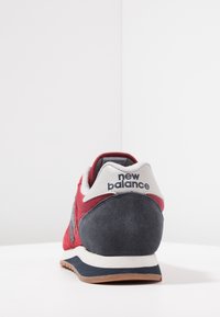 Červené, námořnické modré a bílé tenisky New Balance focené z pohledu paty, ukazujíc�í logo na bílé patní části a textura podešve na bílé ploše.