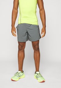 Graue Sportshorts mit lockerer Passform, kombiniert mit einem hellgelben ärmellosen Oberteil. Die Schuhe zeichnen sich durch neonfarbene Akzente und ein aerodynamisches Design aus.