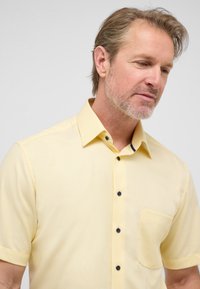 Lichtgele korte mouwen shirt met een gestructureerd patroon, voorzien van een borstzak en donkere knopen langs de sluiting.