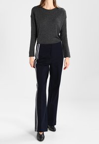 Dunkelgraues Langarmoberteil kombiniert mit marineblauen Schlaghosen mit weißen Seitestreifen. Das Model trägt schwarze Ballerinas. Einfaches, sportliches Design.