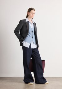 Blazer de cuadros en blanco y negro sobre un chaleco de botones azul claro, pantalones de mezclilla oscuros de pierna ancha y un bolso burdeos de textura suave.