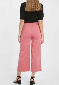 Rosa vida byxor med elastisk midja, tillverkade av mjukt tyg. Kompletteras med svarta klacksandaler och en svart topp med korta ärmar.