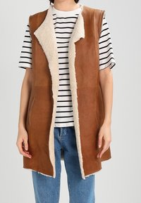 Chaleco marrón de cuero sintético con un suave cuello y forro de piel sintética beige, con apertura frontal, bolsillos laterales y diseño sin mangas.