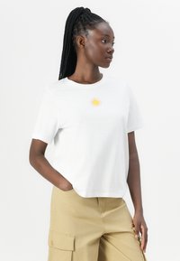 Hvit bomulls t-skjorte med et lite gult solgrafikk på brystet. Løs passform med korte ermer og rund halskrage.