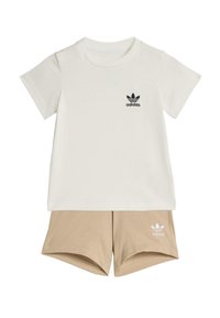 Biała bawełniana koszulka z czarnym logo Adidas oraz beżowe szorty z białym logo Adidas. Obie części mają krótkie rękawy i casualowy krój.
