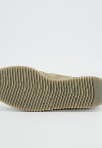 Semelle de sneaker beige avec une surface en caoutchouc texturée, dotée de rainures horizontales et d'un bout arrondi. Aucune marque ou accent supplémentaire visible.