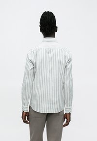 Vaaleansininen ja valkoraidallinen pitkähihainen paita, puuvillakangasta, napillinen hihansuu, kaartuva helma ja takana yläosa detailinä.