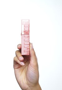 Rosa rektangulär läppprodukt som hålls i en hand, med präglad text och en slät, glansig yta mot en vit bakgrund.