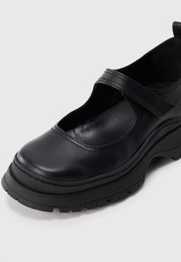 Mustast nahast king ümmarguse ninaosaga, lai rihm jalavõlvi kohal ja tekstureeritud kummitald haarduvuseks. Omab lõigatud mustriga disaini.