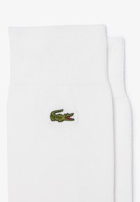Vita bomullssockor med en ribbad textur, som har en liten grön broderad krokodil-logotyp på sidan.