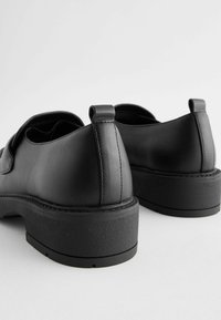 Black leather shoes with a smooth texture, low heel, and a rounded shape. Features a subtle seam detail and a tab at the back for ease of wear.